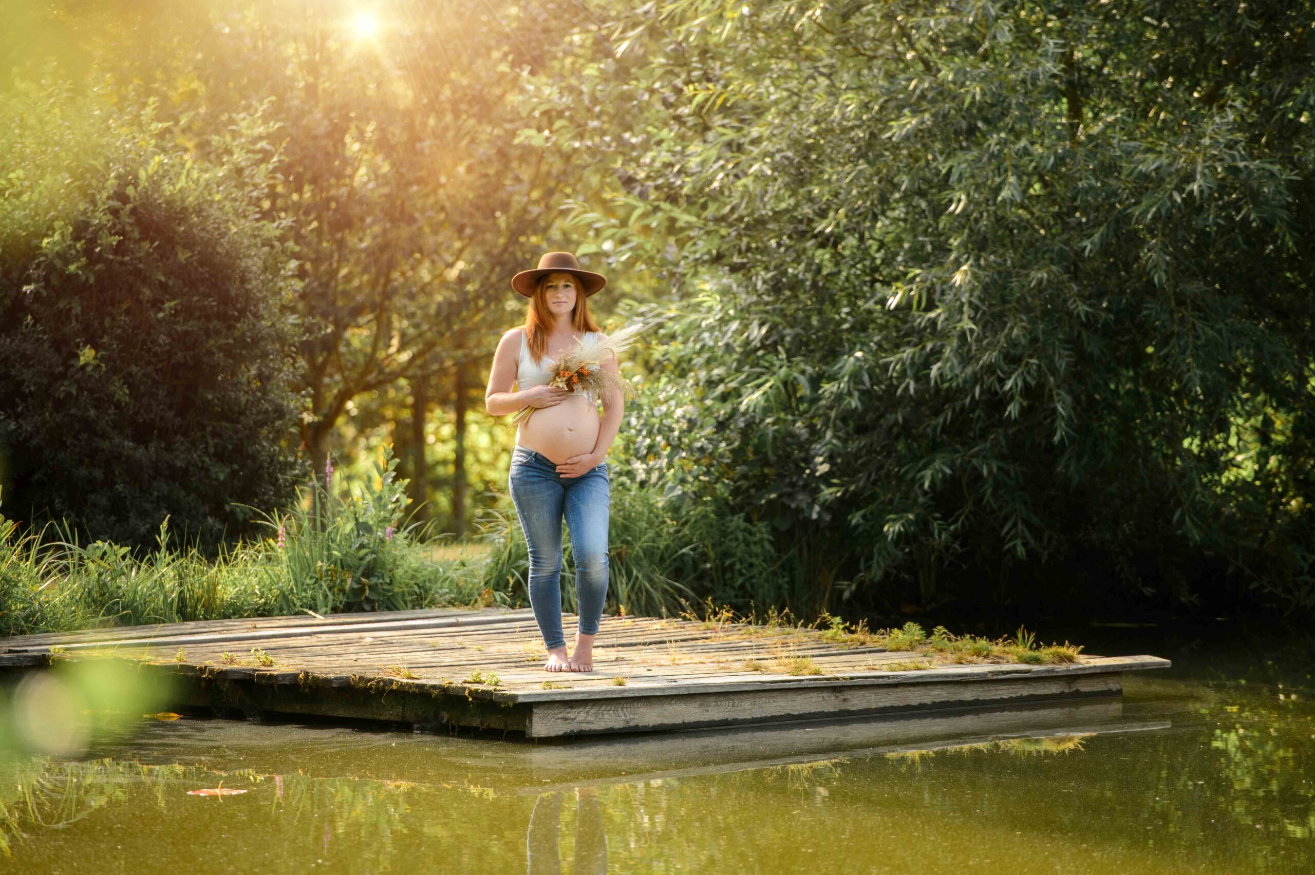 Babybauchshooting am See. Die Schwangere trägt einen Hut , Top und Jeans